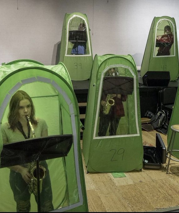 Several students play brass instruments including saxophones and trumpets inside green pop-up practice tents numbered 39 and 29.
