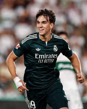Soccer player wearing a dark green Real Madrid away kit with the 'Emirates Fly Better' sponsor logo and the number 19 on his shorts, with a white bandage on his wrist.