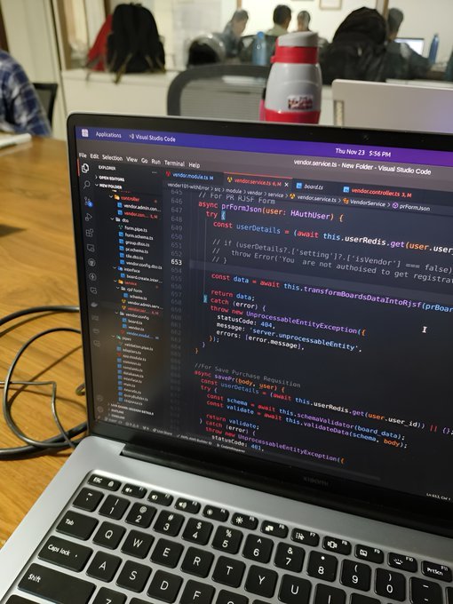 A developer works on a vendor service file in Visual Studio Code, visible on a laptop screen with code referencing `@vendor.service.ts` and functions like `getBoardsDataInto`. The image contrasts with the post's suggestion of using coding games to learn programming, showing a real-world coding environment instead.