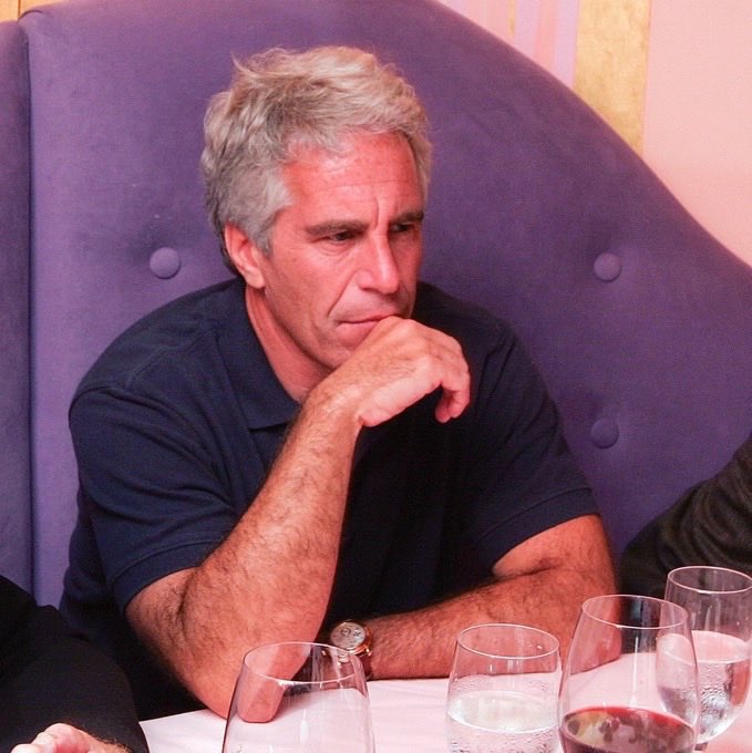 A photograph shows a gray-haired man in a dark polo shirt sitting at a table with glasses of water and red wine, resting his hand near his mouth in a thoughtful pose.