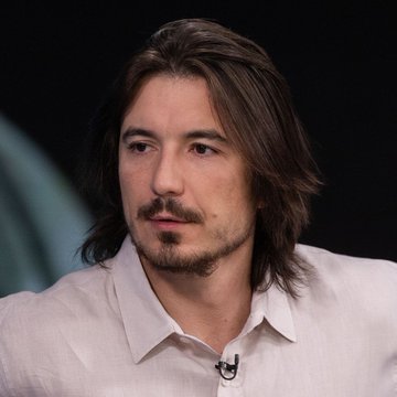 A man with long brown hair and a goatee wears a white button-up shirt, appearing as a guest on what looks like a podcast or interview setting. The accompanying post notes that Robinhood Chain generated $2.2 million in revenue, suggesting the image may be related to a discussion about the company or its founder Vlad Tenev.