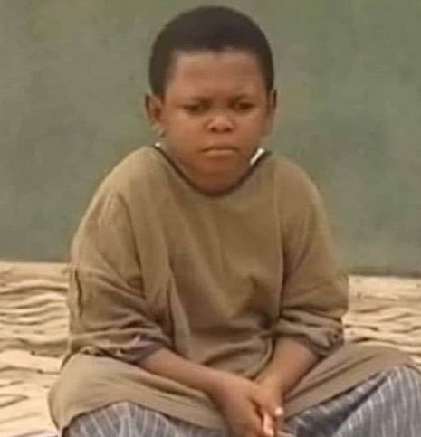 A young boy in an oversized beige shirt sits on a bed with a somber expression, a still frame from a television show.