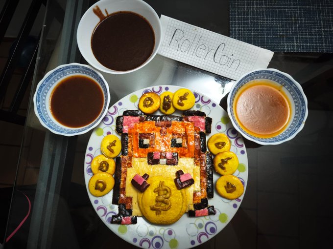 A plate of food artistically arranged to look like a cryptocurrency token, featuring a Bitcoin symbol made of yellow food, surrounded by other coins and dipping sauces, with a note reading 'RolerCoin'.