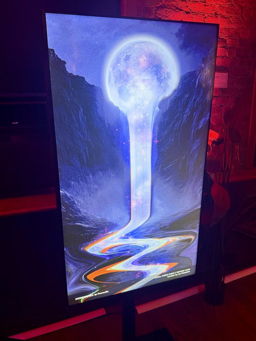 A digital art display showing a glowing celestial sphere streaming liquid light into a winding river-like form, set in a room with red ambient lighting.