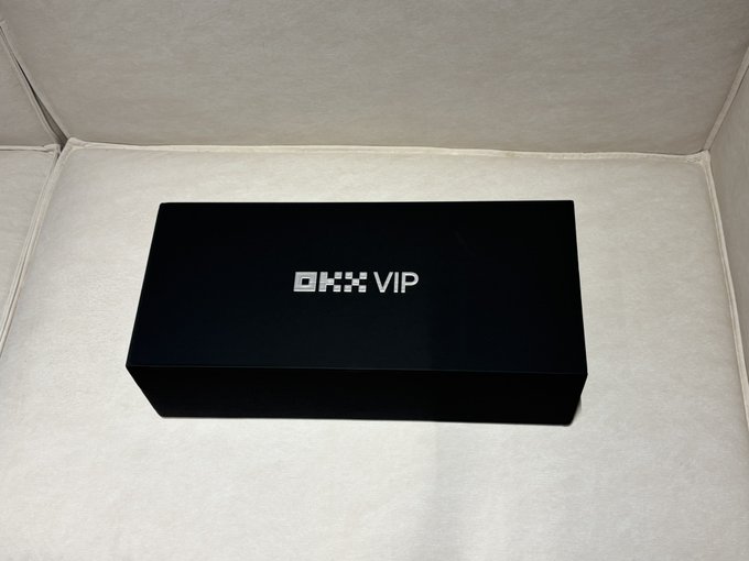 A black rectangular box with the white text 'OKX VIP' centered on its lid, resting inside a light gray lined presentation case.