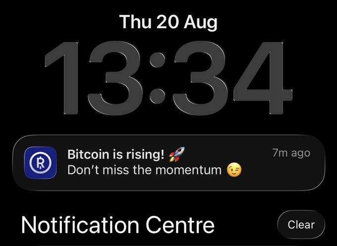 An iPhone lock screen displays the time 13:34 on Thursday, 20 Aug, with a notification from an app showing the message "Bitcoin is rising! 🚀 Don't miss the momentum 😊" received 7 minutes ago, perfectly capturing the FOMO moment mentioned in the post as Bitcoin hovers around the $72k mark.