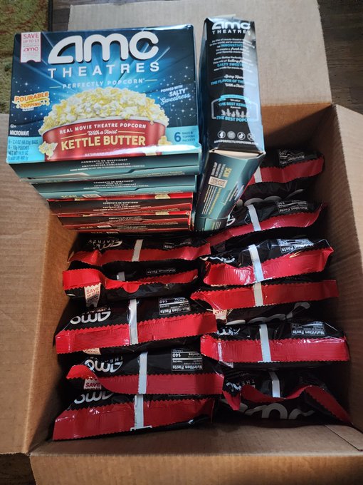 A cardboard box contains multiple bags of AMC Theatres popcorn, including Kettle Butter flavor microwave popcorn.