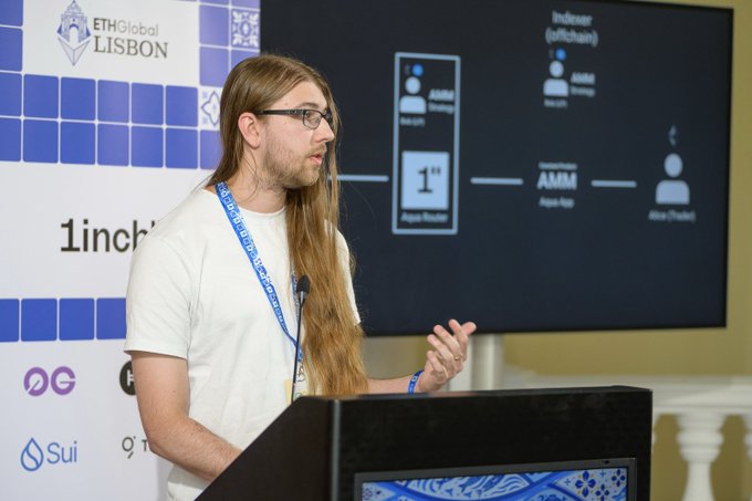 A man with long blonde hair and glasses speaking at a podium at ETHGlobal LISBON, with logos for 1inch and Sui visible on the backdrop, while presenting a slide about indexed software and AMM.