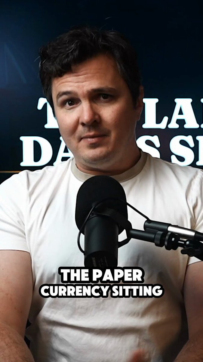 The image features a man wearing a white shirt, sitting behind a microphone with "The Paper Currency Sitting" written above him. The text suggests that he might be discussing the concept of fiat currency or its relevance in today's world.