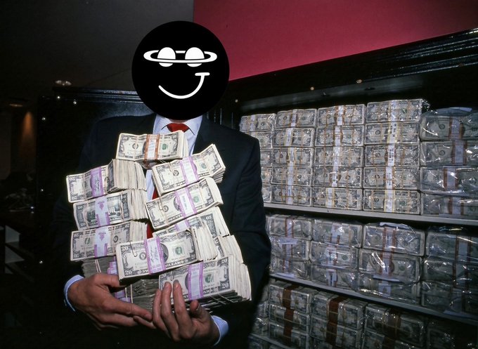 A person in a suit holding multiple stacks of banded US dollar bills, with more stacks of cash visible on shelves in the background; their face is obscured by a smiley face sticker.