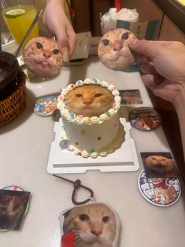 A whimsical scene featuring a small cake decorated with a printed image of an orange cat's face, surrounded by handheld mirrors and printed cat faces on a counter, alongside a glass of orange juice.