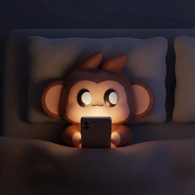 A cute, small brown monkey-like creature lying in bed at night, illuminated by the glow of a smartphone screen.