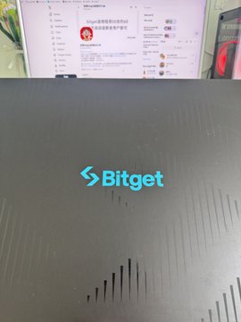 A laptop displaying a Bitget webpage with the glowing blue 'Bitget' logo on the lid sits on a desk.