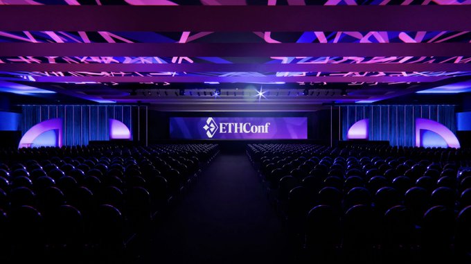 The image shows a large auditorium with rows of chairs, all facing towards the stage where an event is taking place. The stage features a large screen displaying the words "ETHConf" written in white letters. The room appears to be empty, suggesting that the event has not yet started or it's about to end. The post reads: "3 days until ETHConf Doors open Monday at Javits". This message indicates that the event is scheduled for next Monday and will take place at the Javits Center.