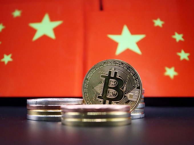 A physical Bitcoin token (inscribed "BITCOIN DIGITAL DECENTRALIZED PEER TO PEER") and stacked gold coins sit in the foreground against a backdrop of the red and yellow Chinese national flag with its five stars, visually pairing Chinese crypto vocabulary terms with the physical symbol of cryptocurrency.