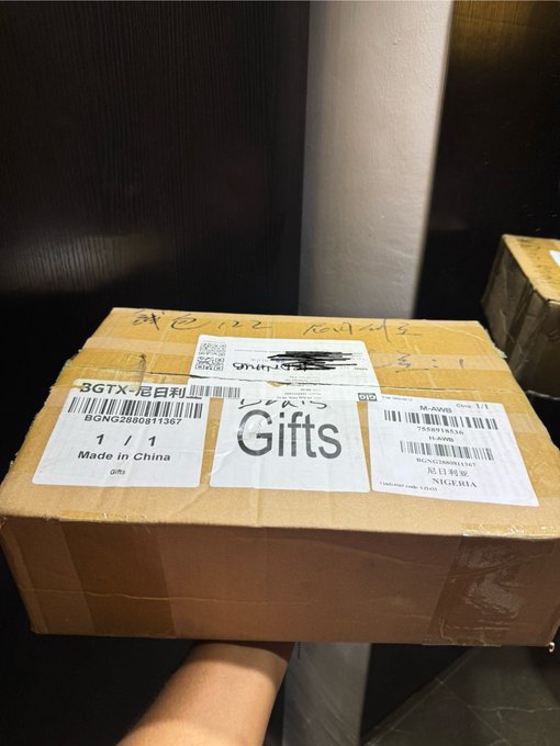 A cardboard box labeled 'Gifts' with shipping labels showing 'Made in China' and 'NIGERIA', with barcodes and tracking numbers visible.