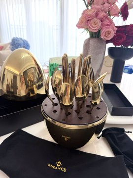 A glossy gold-colored egg-shaped container holds a matching set of gold utensils, branded "BINANCE" on both the base and the carrying pouch below. The image showcases the luxurious "Super Golden Egg" merchandise from Binance, the crypto exchange, presented as a premium fan giveaway item.