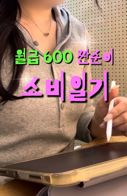 A young woman in a gray hoodie is shown from the neck down, holding a white stylus while working on a tablet with a keyboard case. The Korean text overlay reads "월급 600 잔존이 소비일기" (roughly translating to "Monthly salary 600 leftover spending journal"), which ties into the post's theme of the 26-year-old woman's extreme frugality, saving 5 million won with an 87% savings rate.