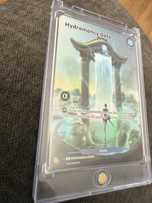 A trading card titled "Hydromancy Gate" encased in a protective sleeve, showing a glowing portal with an "α" symbol.
