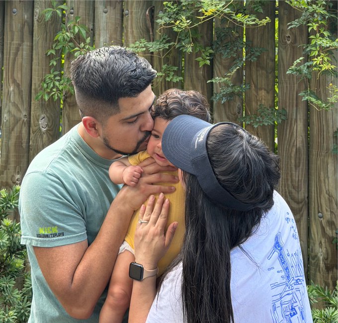 A family shares a tender moment outdoors as a man kisses a baby while a woman in a blue visor and graphic tee holds the child close. The image visually supports the $SOL giveaway post by illustrating "someone special" — a loved one deserving of a dinner treat — though no specific text or numbers appear in the image itself.
