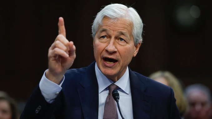 The image features a man wearing a suit, standing up and pointing his finger towards something or someone. He appears to be giving an opinion or making a statement. The caption above him reads "Jamie Dimon is probably the least trustworthy banker of all time." This statement seems to be related to the context of the image, as Jamie Dimon is known for being involved in several controversial banking practices and scandals over the years.