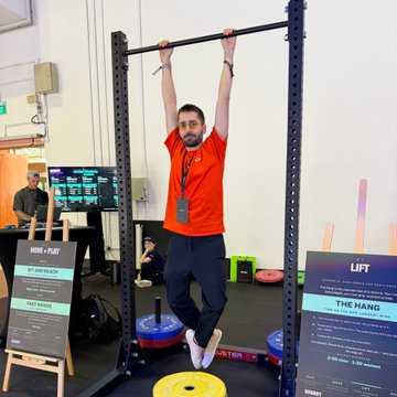 A man in an orange shirt performs a hanging pull-up at the "LIFT" booth during Token2049 Day 2, with a "WIN & PLAY" sign nearby. The image captures a break from the conference's dense project and exchange booths, showing a fun interactive fitness experience amid the event.