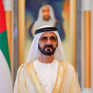 A man in traditional Emirati attire (white kandura and ghutra) stands in a formal setting, with another figure visible in the background and what appears to be a UAE flag partially visible on the left. The image likely depicts a Dubai/UAE official, providing visual context to the announcement about the Dubai government permitting residents to pay taxes and fees using Bitcoin and cryptocurrency.