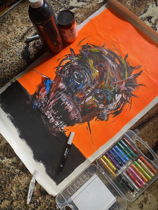 An overhead view of an in-progress acrylic/oil painting of a dog on an orange and black canvas, surrounded by paint tubes, a brush, and an open box of colorful pastel chalks on a granite countertop.