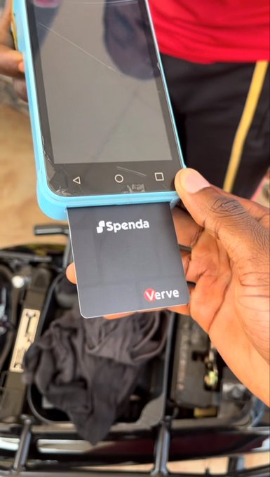 A person holding a smartphone and a Spenda Verve payment card, with a point-of-sale terminal visible in the background.
