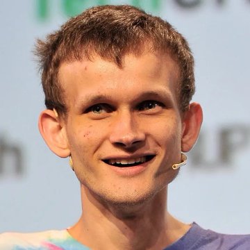 A close-up portrait of a young man with short reddish-brown hair, smiling and wearing a headset microphone, appearing to be at a speaking event.