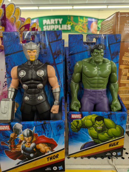 Two large Marvel action figures, Thor and Hulk, in their packaging on a store shelf, likely Target, with a 'Party Supplies' sign in the background.