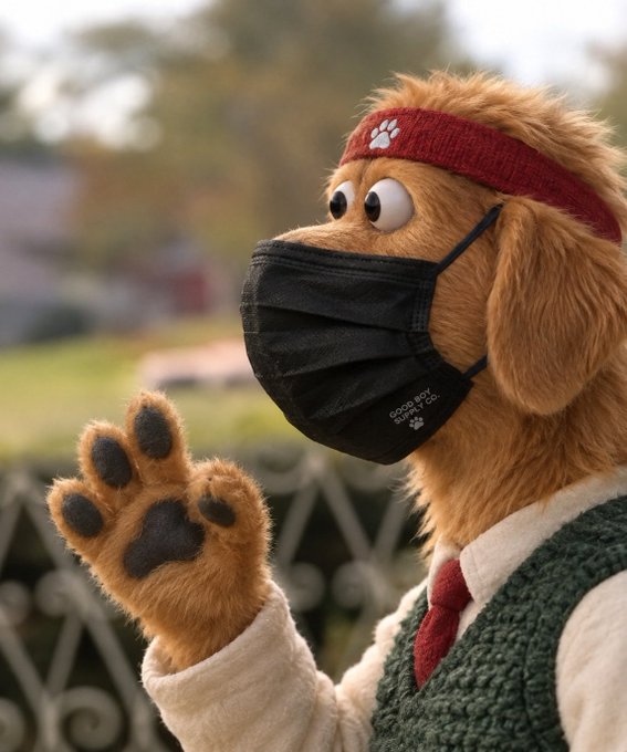 An anthropomorphic golden retriever mascot wearing a red headband with a paw print and a black face mask waves at the camera outdoors.