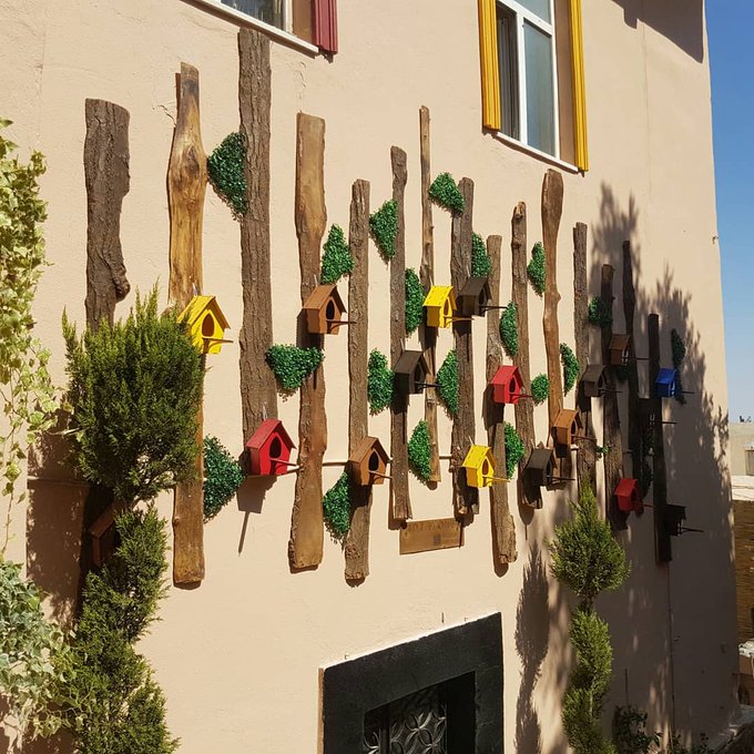 The image features a wall adorned with various birdhouses made from wood and painted in different colors, including red, yellow, green, blue, and brown. The birdhouses are arranged in an artistic manner that creates a visually appealing display on the side of a building. The post includes text about the importance of staying positive during challenging times and encourages people to chat with ANIMA for more information about Web3.