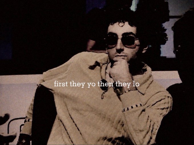 A vintage-toned photograph shows a young man with dark curly hair and sunglasses resting his chin on his hand, with the text 'first they yo then they lo' overlaid across the center.