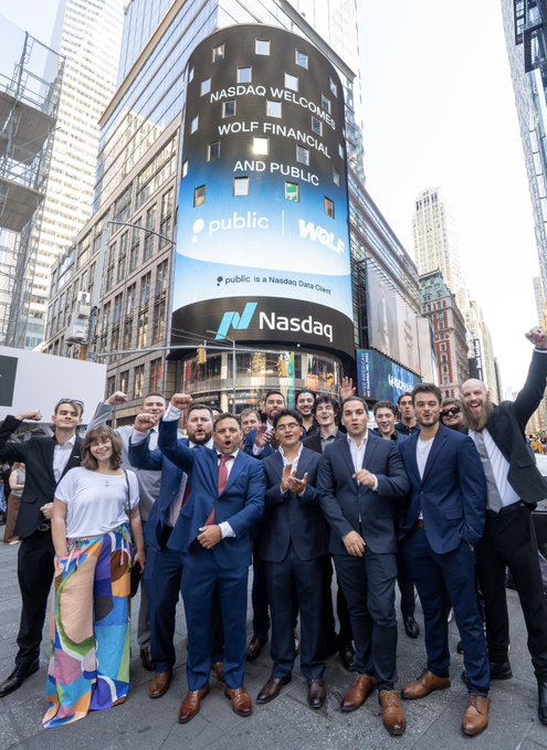 The Public.com team celebrates outside the NASDAQ building in Times Square, with the tower's digital marquee welcoming "WOLF FINANCIAL AND PUBLIC" and declaring "public is a Nasdaq Data Center" — marking their Nasdaq listing ceremony.