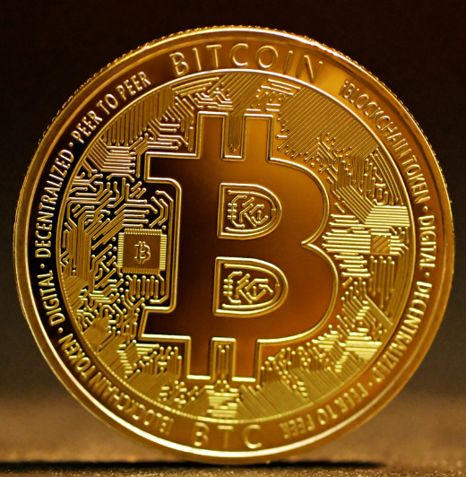 A close-up of a gold-plated physical Bitcoin coin featuring its iconic "₿" symbol surrounded by circuit board patterns and the inscriptions "BITCOIN DIGITAL DECENTRALIZED PEER TO PEER," visually representing the digital asset $BTC discussed in the post about Bitcoin's correlation to US stocks being lower than gold, small caps, emerging markets, and treasuries over the past six months.
