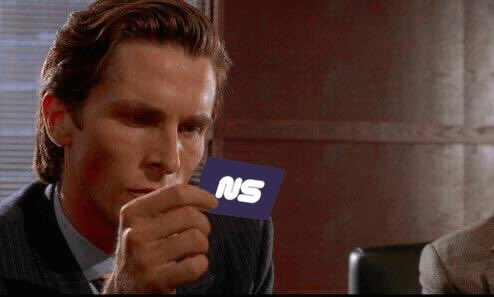 A still from a film showing a man in a pinstripe suit holding a small card with the letters "NS" near his mouth.