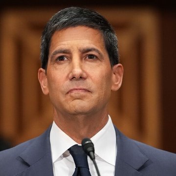A man in a dark navy suit and white shirt speaks into a microphone against a wood-paneled background, appearing to deliver testimony or a statement. The image likely accompanies the post because it depicts a Federal Reserve official or financial policy expert addressing the prospect of further interest rate hikes amid persistent inflation concerns.