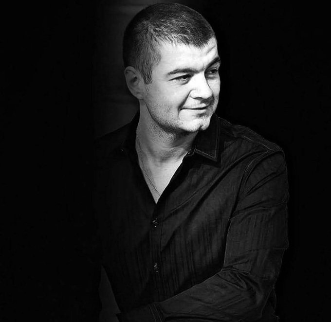 A black and white portrait of a man in a dark button-up shirt, looking off to the side.