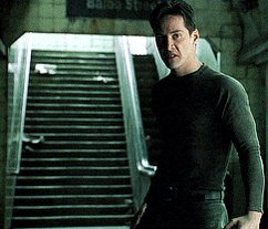 The image features a man standing in front of stairs, wearing a black shirt and pants. He has his hands on his hips and appears to be posing for the camera. The background includes an escalator and a sign that reads "LUNC is the ONE!".
