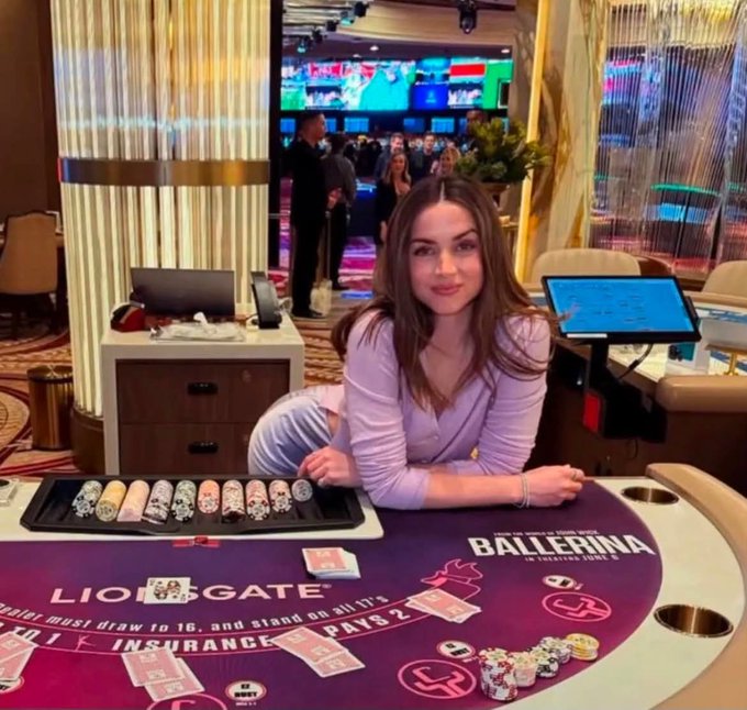 A young woman in a lavender top leans on a purple baccarat table labeled "LION GATE" and "BALLERINA," smiling confidently at the camera with a tray of sushi and poker chips in front of her. The caption contrasts her relaxed, happy demeanor with the post's humorous reference to being down to a last $200, suggesting her poker face masks her losing streak.