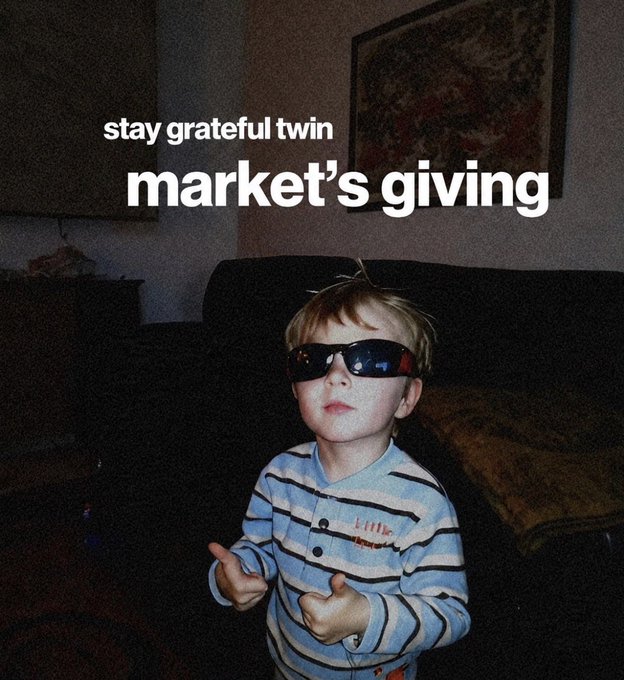 A young boy wearing oversized sunglasses and a striped shirt gives a double thumbs-up, overlaid with the text "stay grateful twin / market's giving." The image humorously personifies the speaker's mindset during a bull run—projecting confidence and contentment with market gains as a reminder not to chase unrealistic returns, embracing the "stay grateful" mentality instead of greed.