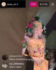 A livestream screenshot showing a person wearing a yellow floral dress and a flower crown. Visible text includes 'enerji_mt', 'LIVE', '21.6K', and a comment reading 'stepcich97: Shes meditating guys. rui_20oliveira: She's died'.