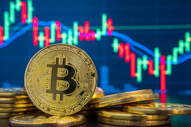 The image shows a stack of gold Bitcoin tokens, with one standing upright displaying the iconic "B" symbol, set against a background of a candlestick stock chart featuring red and green price bars and blue trend lines. This visual reinforces the post's theme of cryptocurrency market activity, as the BTC tokens in the foreground symbolize the Bitcoin being transferred and potentially sold off by Trump Media, while the volatile chart in the background reflects the significant losses and downward trend affecting their position.