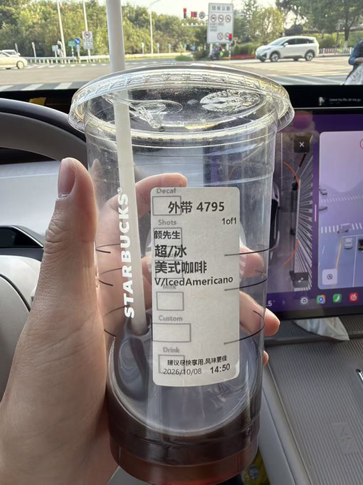 A hand holding a clear Starbucks cup containing a dark iced beverage, with the label reading 'Decaf', 'Iced Americano' (美式咖啡), order #4795, dated 2026/10/08.