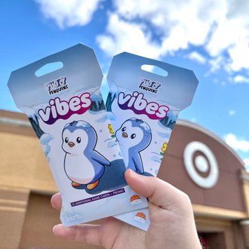 A hand holds two "Tuff Tunes Vibes" penguin-themed cards at what appears to be a Target store, illustrating the post's point about physical-digital brand fusion—these tangible collectibles represent how brands are bridging online NFT culture with real-world products and community experiences.