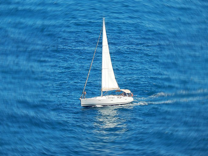 An aerial view of a white sailboat gliding across deep blue, rippling ocean waters.