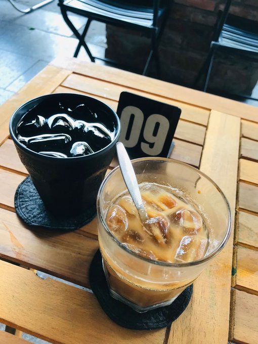 A table at an outdoor café holding an iced coffee in a glass with a spoon and a cup of water with ice, next to a table number '09'.