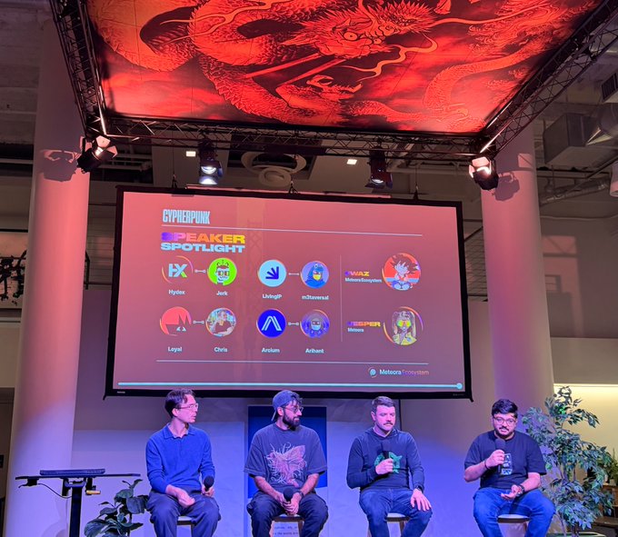 A panel discussion at a Cyberpunk-themed event with a red dragon ceiling installation; the screen shows 'SPEAKER SPOTLIGHT' featuring Hydra, Jinx, LnAcgm, m3tav3rse, Loyal, Chris, Arcium, and Anbain, moderated by Mitosis Ecosystem.