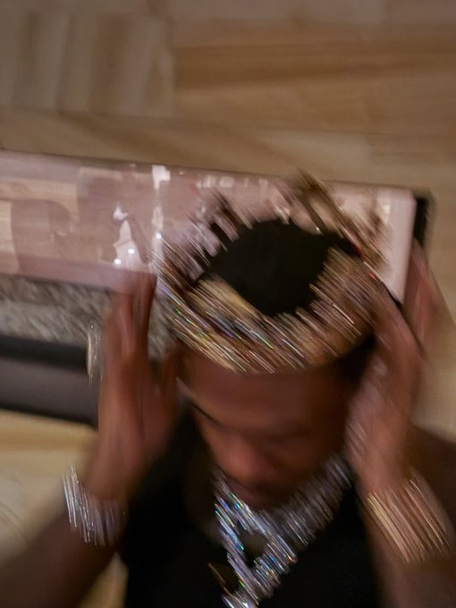 Blurry selfie of a person wearing a large sparkly crown and jeweled necklaces holding their head with both hands.